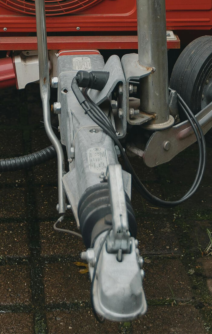 Nahaufnahme einer Anhängerkupplung mit elektrischem Anschluss und einem kleinen schwarzen Rad auf einer gepflasterten Fläche.