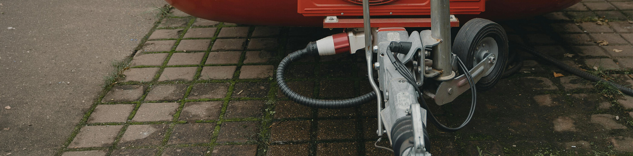 Nahaufnahme einer Anhängerkupplung mit elektrischem Anschluss und einem kleinen schwarzen Rad auf einer gepflasterten Fläche mit Moos.
