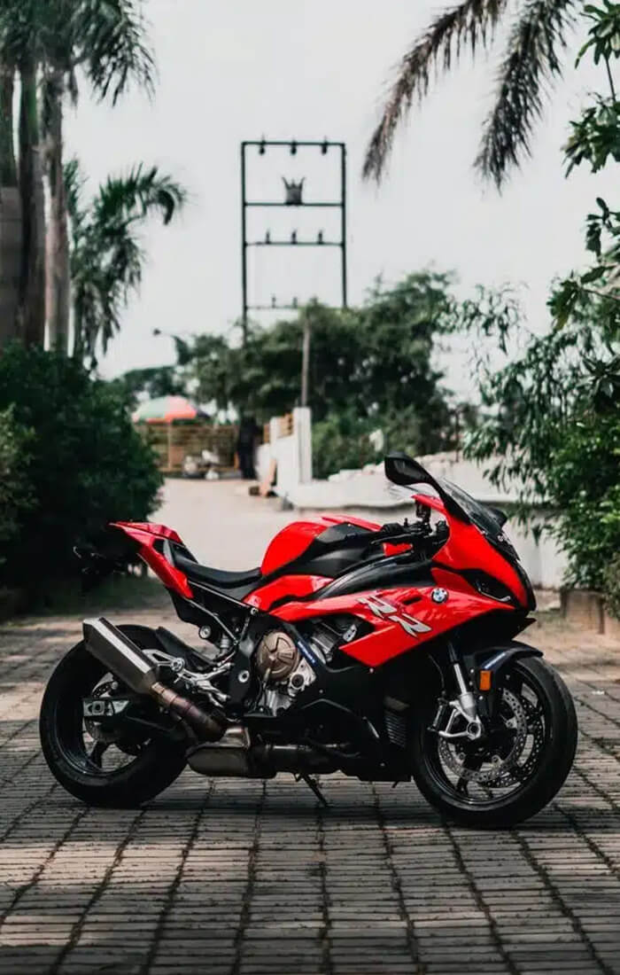 Ein rotes BMW-Sportmotorrad, das auf einem gepflasterten Weg steht, umgeben von grünen Büschen und Mauern.