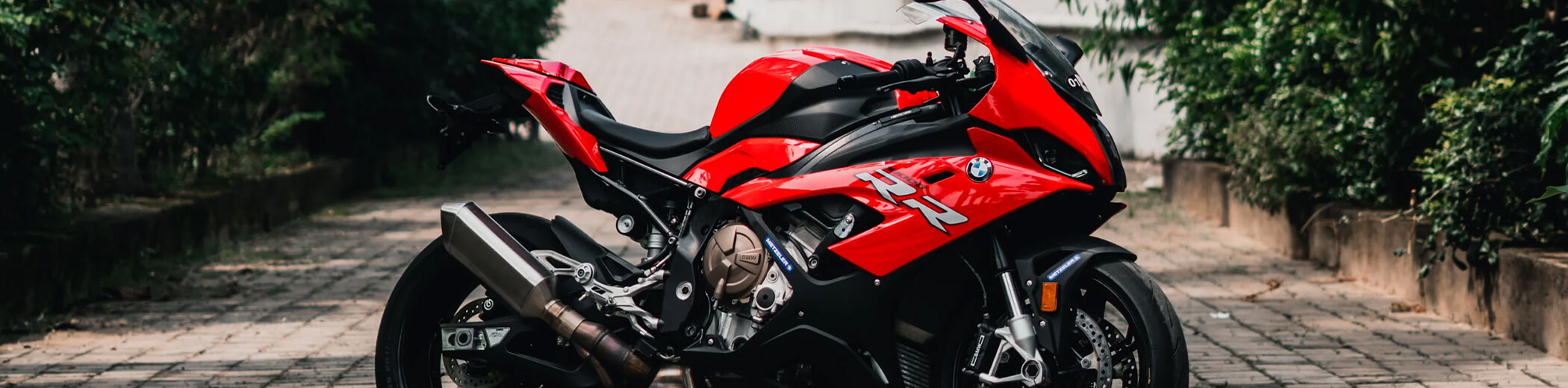 Ein rotes BMW-Sportmotorrad, das auf einem gepflasterten Weg steht, umgeben von grünen Büschen und Mauern.