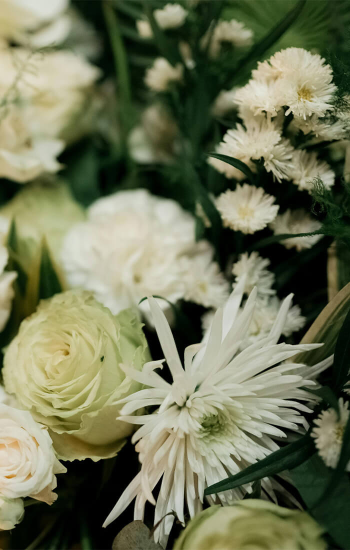 Nahaufnahme von weißen und hellgrünen Blüten, darunter Rosen und Chrysanthemen, umgeben von grünem Laub.