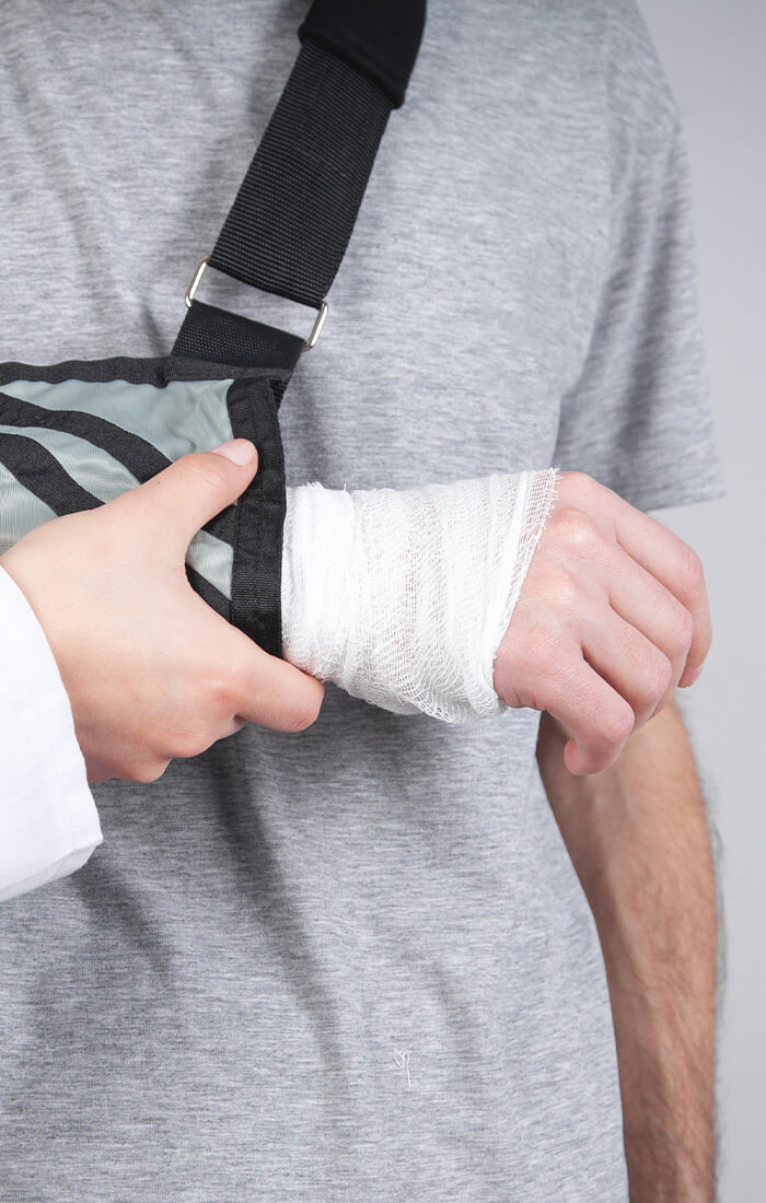 Ein Arzt richtet die Armschlinge einer Person mit bandagierter Hand und leistet medizinische Hilfe und Unterstützung.